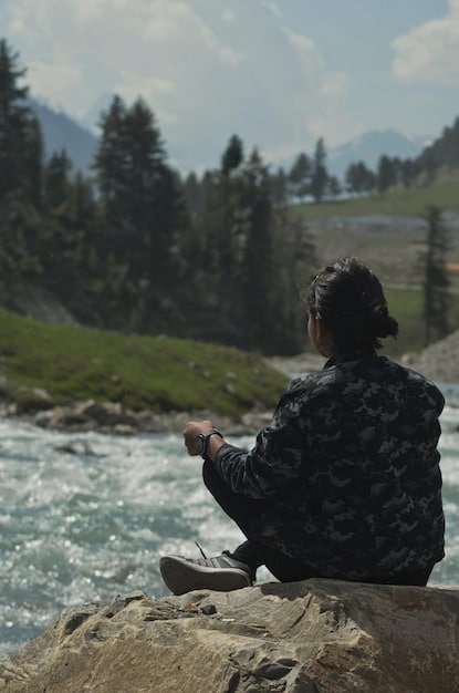 A person practicing Qigong meditation outdoors, with a serene lake and mountains in the background. The image captures the tranquility and natural setting often associated with the practice.
